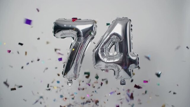 Silver balloon number 74 for birthday or anniversary party. White background with falling confetti