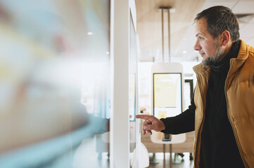 Man using self-service touchscreen kiosk in modern restaurant, interacting with digital ordering system, choosing items on interactive display, concept of technology, automation, and customer convenie