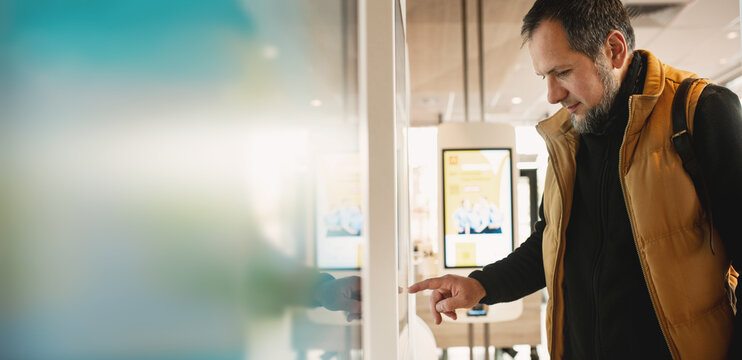 Man using self-service touchscreen kiosk in modern restaurant, interacting with digital ordering system, choosing items on interactive display, concept of technology, automation banner copy space