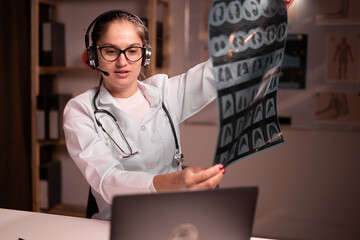 Telemedicine concept. female doctor talking with patient on laptop and shows x-ray to screen. Medical worker working during night shift in hospital