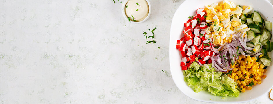Salad with cabbage, crab sticks, eggs, cucumber and red onions in white bowl. Healthy salad. Top view