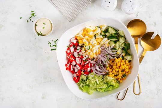 Salad with cabbage, crab sticks, eggs, cucumber and red onions in white bowl. Healthy salad. Top view