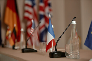Conference table displaying microphones, glass bottles, and small national flags including France, United States, Germany, and United Kingdom, representing international diplomatic meeting