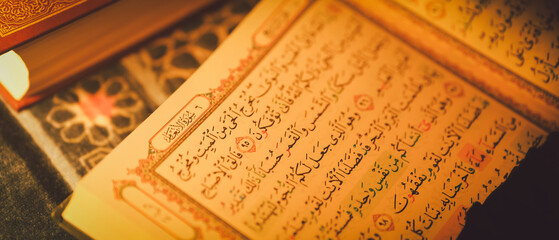 Close-up of open Quran with Arabic text on prayer rug, illuminated by warm light, symbolizing Islamic faith, spirituality, and daily devotion in Muslim religious practice.