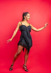 Woman enjoying a lively salsa dance in a black fringe dress on a red background