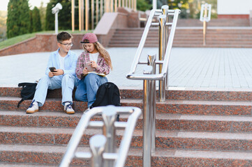 Schoolchildren using smartphones and studying outdoors on campus stairs