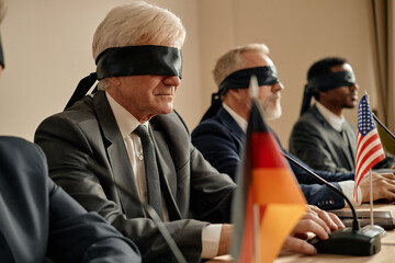 Group of middle aged and senior men of diverse ethnicities sitting at conference table wearing...