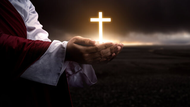Jesus Christ raising his hand and praying with the Christian cross with dark dramatic sky background. Concept of Christianity, religious, faith, Jesus, or belief