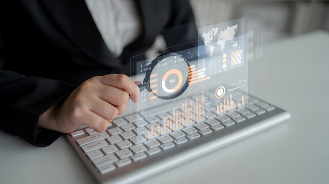 A business professional is reviewing digital data trends on a transparent dashboard while typing on a keyboard in a contemporary office setting with engaging visuals. Scalp