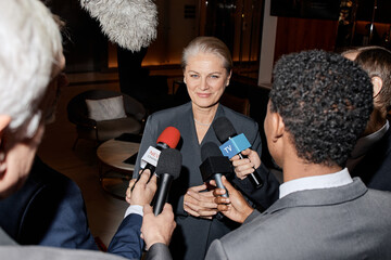 Caucasian middle aged woman standing in formal attire being interviewed by group of male...