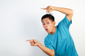 A young Asian man smiling cheerfully, feeling happy and pointing to the side, showing object in copy space