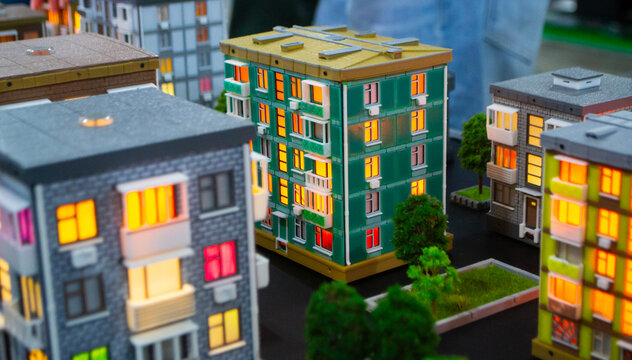 Prototype building printed on 3D printer from melted plastic. 3D-printed building prototype. A house created on 3D printer with green walls, gray roof, and illuminated windows and balconies.