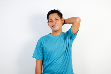 Portrait of a young Asian man dressed in a blue shirt, smiling confidently while striking a casual pose with one hand resting on his neck.  © Ichsan Gallery