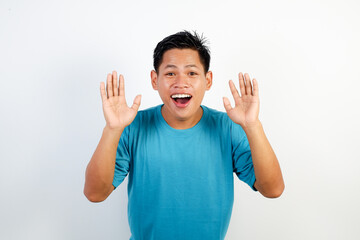 A young Asian man wearing a blue T-shirt raises his hands in a surprised, playful pose.