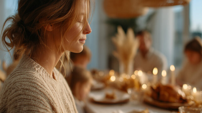 Woman with closed eyes, praying, feeling thankful for her family. Thanksgiving dinner table. Concept of gratitude, family.