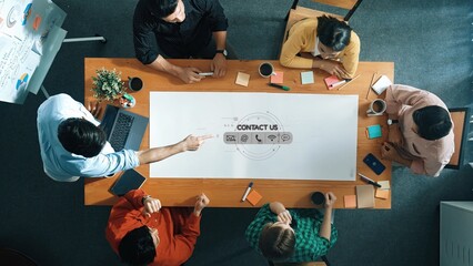 This image captures a diverse group of professionals engaged in a brainstorming session at a large wooden table, showcasing collaboration and creativity in a modern office setting. Raster