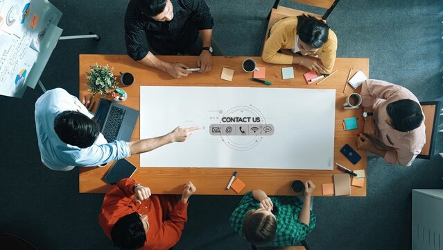 This image captures a diverse group of professionals engaged in a brainstorming session at a large wooden table, showcasing collaboration and creativity in a modern office setting. Raster