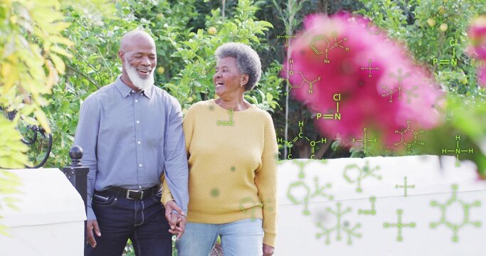 Walking couple holding hands, talking on garden path in blue shirt, mustard sweater with white wall