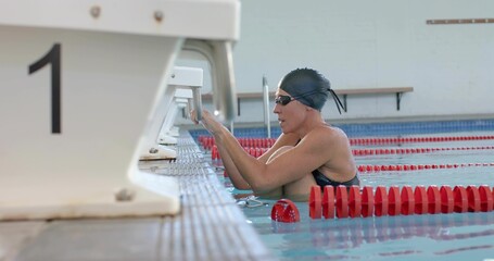 Holding swimmer wearing black cap and goggles at pool edge near starting block 1, copy space