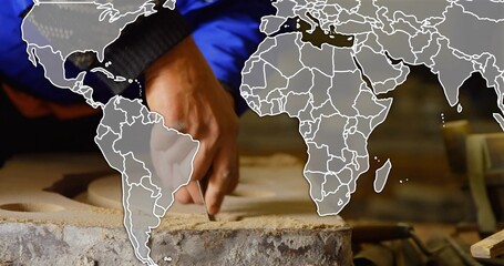 Carving hand working on clay slab with pits at bench, blue-jacket black-cuff, chisel, map-overlay