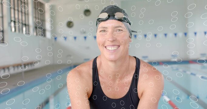 Smiling woman swimmer leaning on pool edge, wearing black one-piece swimsuit, swim cap, lane ropes