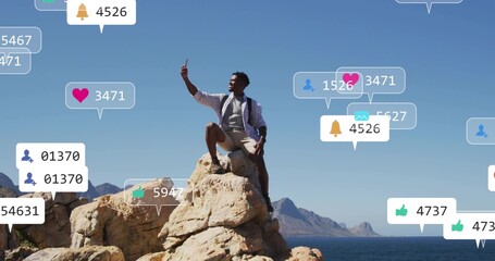 Taking smartphone selfie, hiker on rock by sea wearing backpack, floating notifications, mountains