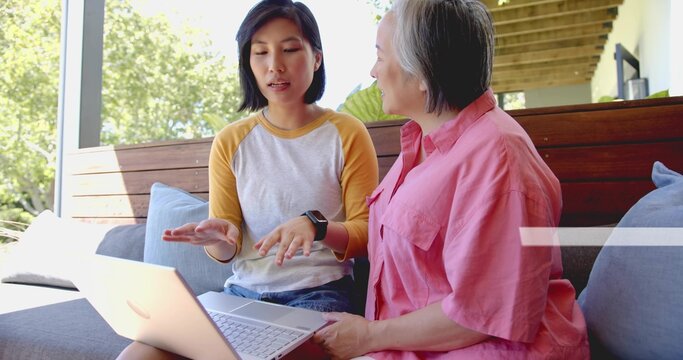 Showing two Asian women gesturing over laptop on porch, wearing raglan tee, pink shirt, smartwatch