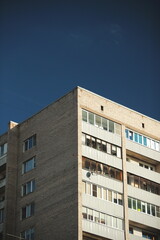 Close-up of old Soviet style residential apartment facade with brick and metal panels against blue sky.