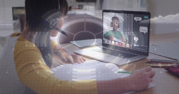 Writing child in yellow long-sleeve shirt studying with pencil at home desk, with laptop and HUD