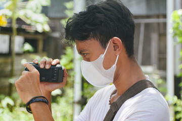 Young Man Filming with Camcorder While Wearing Face Mask Outdoors. Captures modern lifestyle, content creation, and everyday documentation in a natural environment.