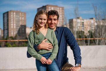 Fototapeta premium Father and daughter posing together, embracing and smiling in an urban outdoor setting