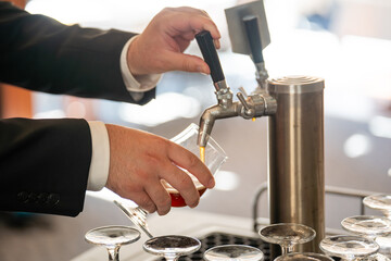 A bartender, dressed in a formal suit, is meticulously pouring a golden amber beer from a...