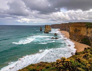 Coastal view features rock formations rising from turquoise ocean waters. A sandy beach extends between cliff faces under cloudy skies