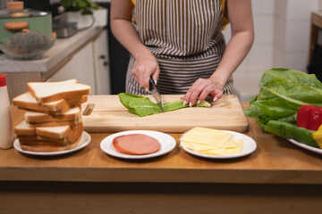 Close-up of hands cutting fresh lettuce with a knife on a wooden chopping board in the kitchen