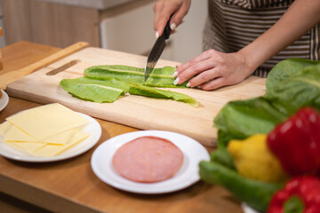 Close-up of hands cutting fresh lettuce with a knife on a wooden chopping board in the kitchen