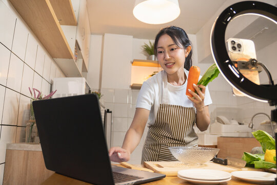 Asian food vlogger showing ingredients, using a laptop and smartphone on a ring light to host a cooking live stream