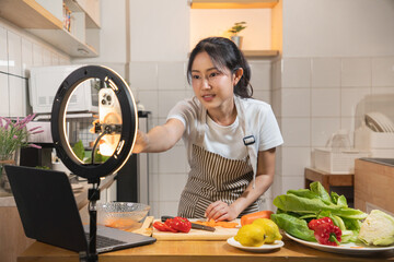 Asian woman cooking and recording a video using a smartphone on a ring light for a food vlog or livestream