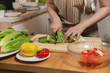 Close-up of hands slicing fresh lettuce on a wooden chopping board while preparing a healthy salad