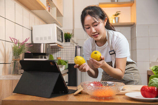 Asian woman cooking while following a recipe or teaching a lesson on a tablet in her kitchen
