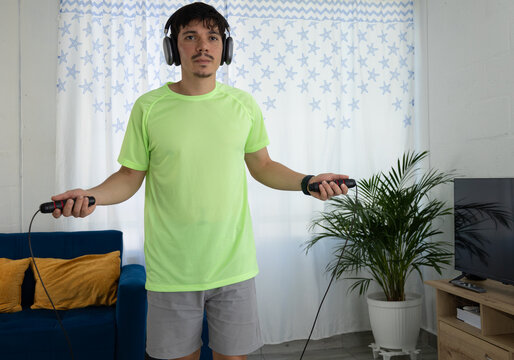 Athletic man exercising with a jump rope in the living room of his home while listening to music with headphones. Concept of energy, fitness, technology, and a healthy lifestyle - Powered by Adobe