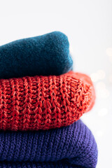Close-up of a stack of colorful sweaters with blurred holiday lights.