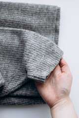Woman holding gray sweater with pilling on white background.