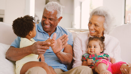 Grandparents Sitting On Sofa At Home Playing With Baby Granddaughters