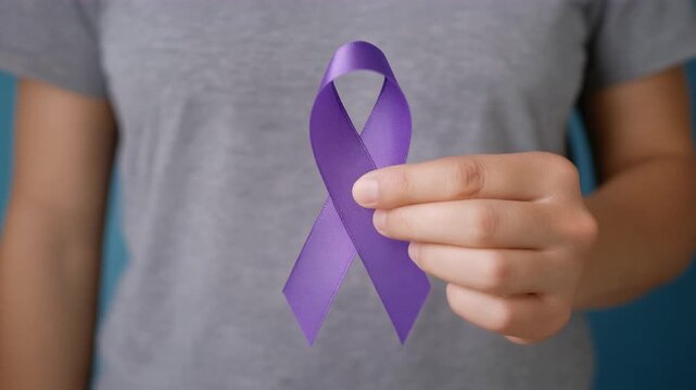 Hand holding purple awareness ribbon. Pancreatic cancer, Alzheimer disease, epilepsy. Close-up.