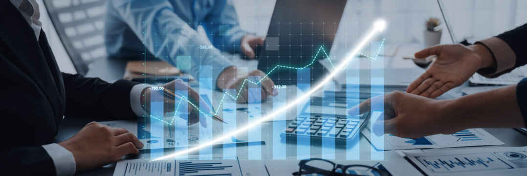 Business professionals collaborate in a modern office, analyzing financial data and discussing growth strategies using laptops, calculators, and charts. Axiom - Powered by Adobe