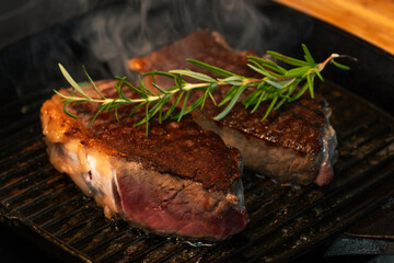Grilled Beef Steaks with Rosemary Sizzling on a Hot Grill Pan. Juicy, seared meat with grill marks and smoke, ready to be served. Perfect for restaurant and gourmet cuisine.
