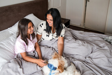 A woman and a girl are laying on a bed with a dog