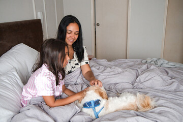 A woman and a girl are petting a dog on a bed