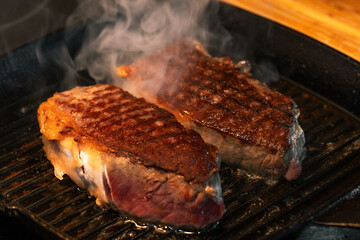 Juicy grilled beef steaks sizzling on a cast iron grill pan. Hot steak with grill marks and smoke...