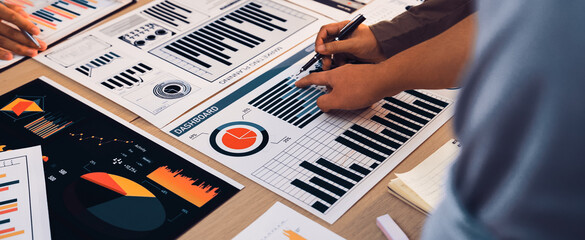 Professionals engage in a collaborative effort over various business charts and reports, focusing on data analysis and strategic planning in a modern office environment. SACTR